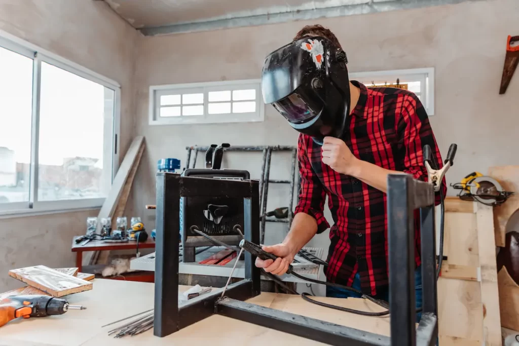 Un soudeur travaille sur la fabrication de mobiliers d'atelier.